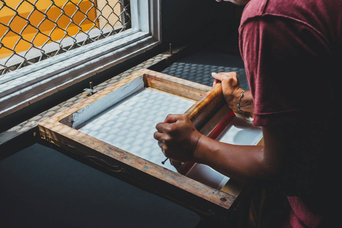 A close-up of a hand pulling a squeegee across a screen during screen printing t shirts diy